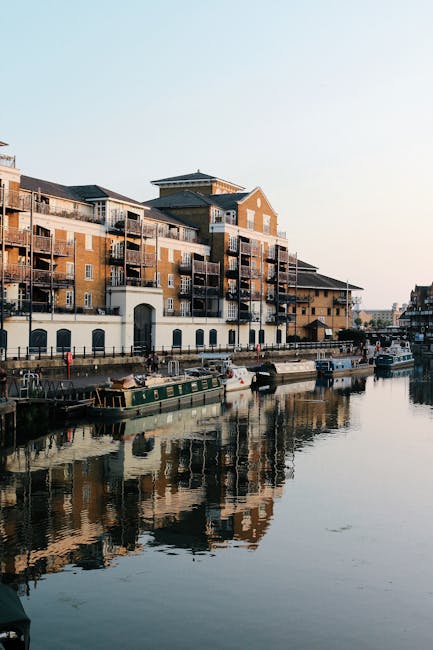 Two professional movers from Storage Hackney Wick are engaged in a home relocation task, loading a large piece of furniture wrapped in green protective fabric into the open rear of a white moving van.
